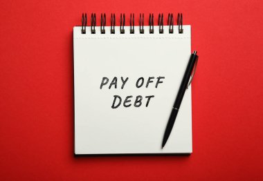 Notebook with phrase Pay Off Debt and pen on red background, top view