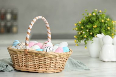 Easter basket with many painted eggs on white marble table
