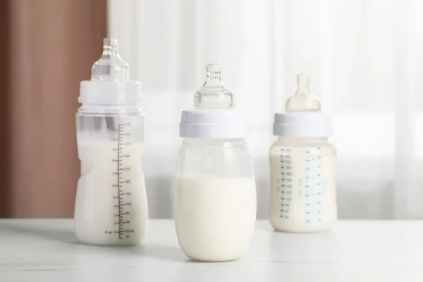Feeding bottles with milk on white table indoors