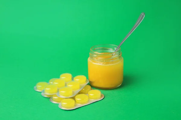 Blisters with cough drops and honey on green background