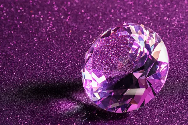 Beautiful shiny diamond on purple glitter background, closeup. Space for text