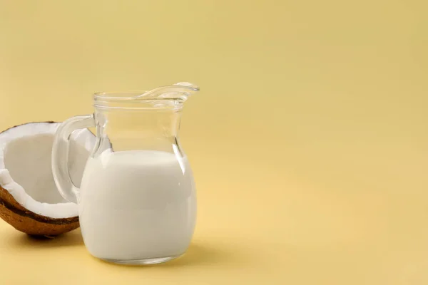 Glass jug of delicious vegan milk and coconut on yellow background, space for text