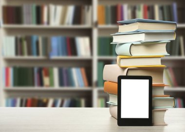 Stack of hardcover books and modern e-book on wooden table in library. Space for text