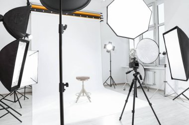Tripod with camera, bar stool and professional lighting equipment in modern photo studio