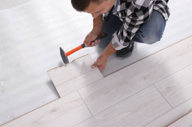 Professional worker using hammer during installation of new laminate flooring, closeup