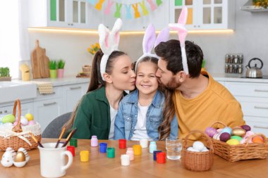 Happy family with Easter eggs at table in kitchen