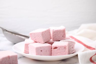 Plate of delicious sweet marshmallows with powdered sugar on white marble table, closeup