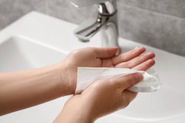 Woman wiping hands with paper towel in bathroom, closeup