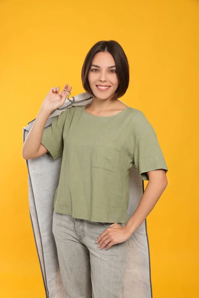 Woman holding garment cover with clothes on yellow background. Dry-cleaning service