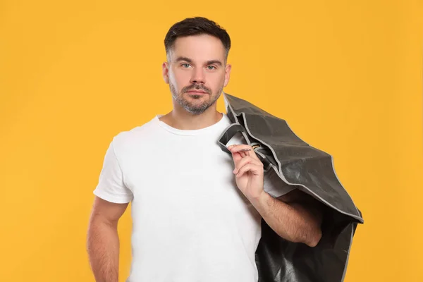 Man holding garment cover with clothes on yellow background. Dry-cleaning service