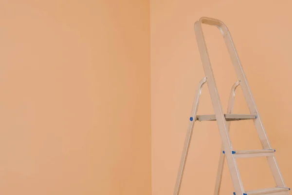 Ladder near pale orange wall, space for text. Room renovation