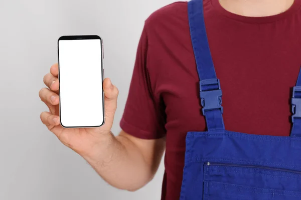 Professional repairman in uniform with phone on white background, closeup