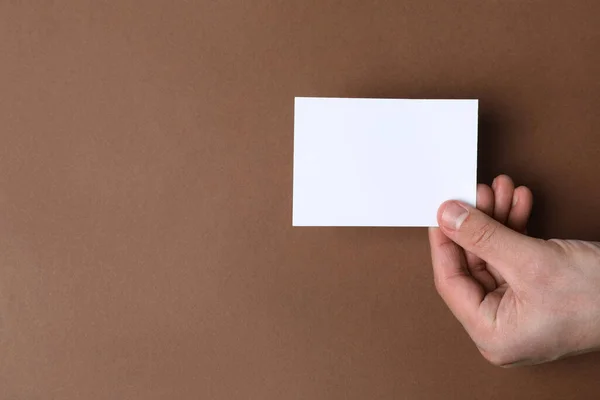 Man holding paper card on brown background, top view. Mockup for design