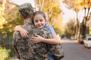 Daughter hugging her father in Ukrainian military uniform on city street. Family reunion