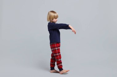 Boy in pajamas sleepwalking on light gray background