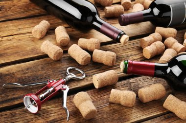 Bottles with wine, corkscrew and corks on wooden table