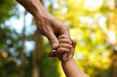 Daughter holding father's hand outdoors, closeup. Happy family