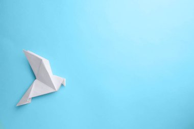 Origami art. Beautiful handmade paper bird on light blue background, top view. Space for text