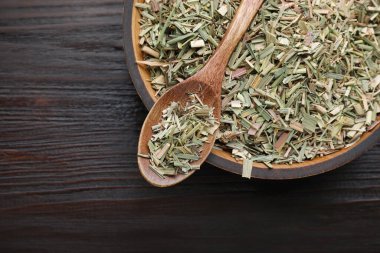 Bowl with aromatic dried lemongrass and spoon on wooden table, top view