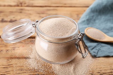 Glass jar and spoon with active dry yeast on wooden table, closeup
