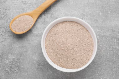 Bowl and spoon with active dry yeast on light grey table, closeup, flat lay