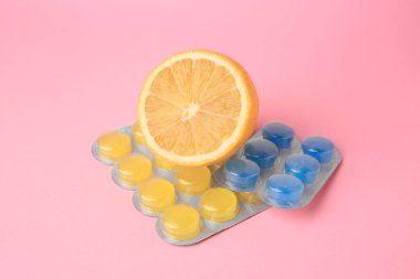Blisters with cough drops and fresh lemon on pink background