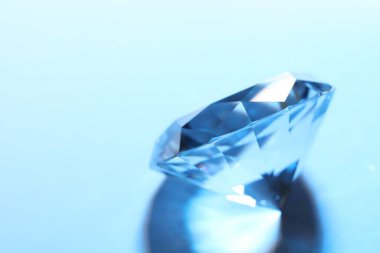 Beautiful dazzling diamond on blue background, closeup. Space for text