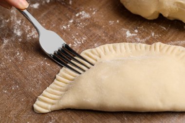 Woman making chebureki at wooden table, closeup