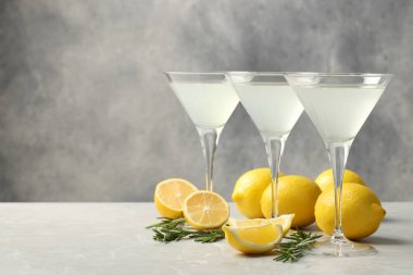 Martini glasses of refreshing cocktail, lemon and rosemary on light grey textured table. Space for text