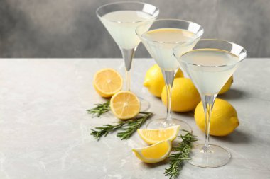 Martini glasses of refreshing cocktail, lemon and rosemary on light grey textured table. Space for text