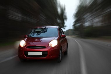 Red car driving at high speed on asphalt road outdoors, motion blur effect