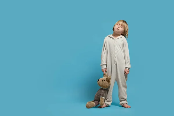 Boy in pajamas with toy bear sleepwalking on light blue background, space for text