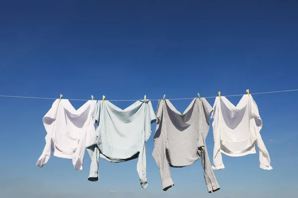 Washing line with drying clothes and clothespins under blue sky, space for text