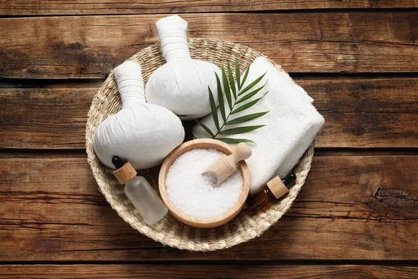 Composition with herbal massage bags and other spa products on wooden table, top view
