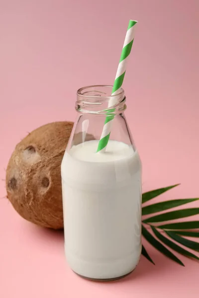Glass bottle of delicious vegan milk, coconut and leaf on pink background