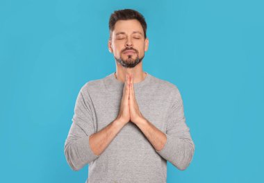 Elleri sıkıca bağlı bir adam turkuaz arka planda dua ediyor.