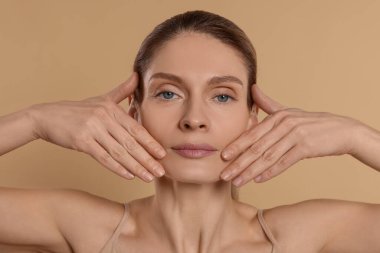 Woman massaging her face on beige background clipart