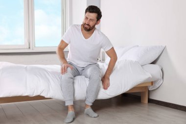 Man suffering from leg pain on bed at home