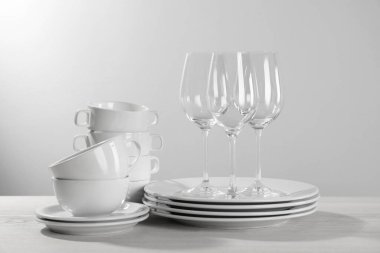 Set of clean dishware and glasses on white wooden table against light background