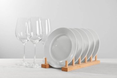 Set of clean plates and glasses on white wooden table against light background