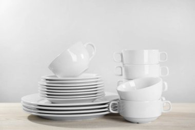 Set of clean dishware on white wooden table against light background