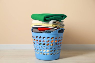 Plastic laundry basket with clean clothes on floor near beige wall