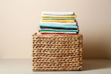 Wicker laundry basket with clean clothes on floor near beige wall