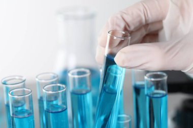 Scientist taking test tube with light blue liquid in laboratory, closeup