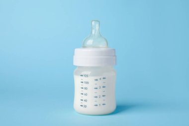 One feeding bottle with milk on light blue background