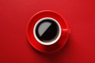 Cup with aromatic coffee on red background, top view