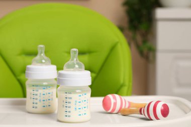 High chair with feeding bottles of infant formula and toy maracas on white tray indoors