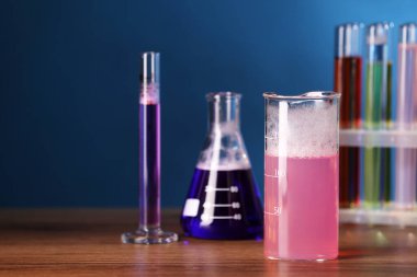 Laboratory glassware with colorful liquids on wooden table, space for text. Chemical reaction
