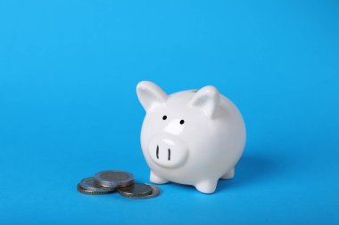Ceramic piggy bank and coins on light blue background. Financial savings