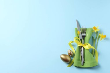 Cutlery set, Easter eggs and narcissuses on light blue background, flat lay with space for text. Festive table setting